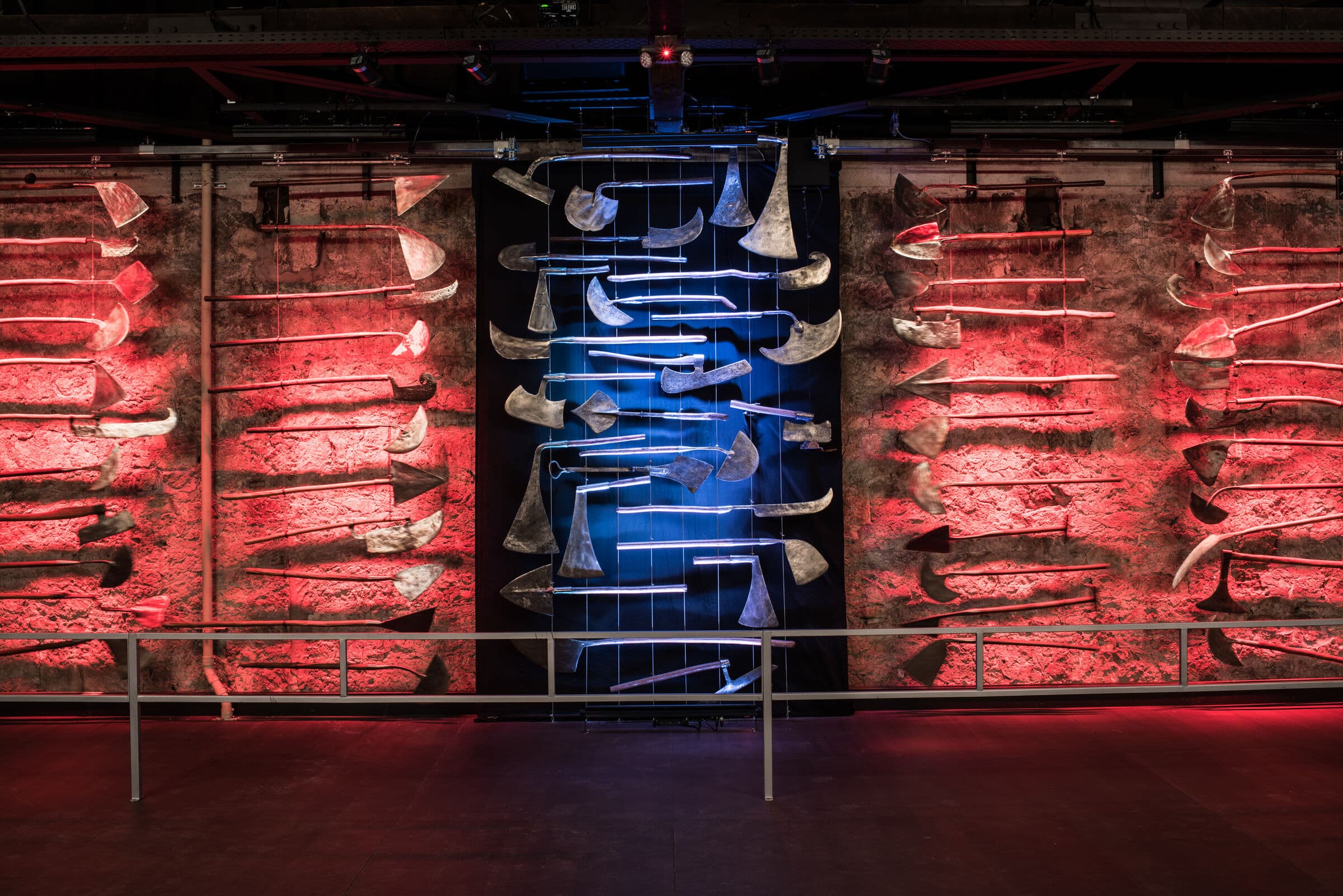 A wall of 19th-century pruning hooks, axes and vineyard implements, lit red and blue, in the Buena Vista tool museum